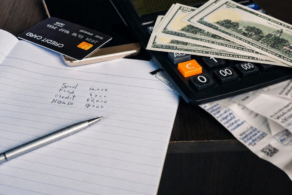 A desk setup with a calculator, notes, and money for conducting a monthly income review.
